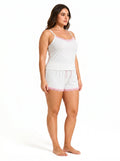 Woman wearing a white ribbed camisole and shorts pajama set with pink lace trim and bow details, side view, left.