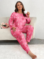 Woman wearing a pink long-sleeved pajama set with an all-over heart print, sitting on a sofa and holding a cup.