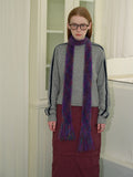 Woman wearing a gray sweatshirt, maroon skirt, white socks, black boots, and a purple and green fuzzy scarf with fringed ends.