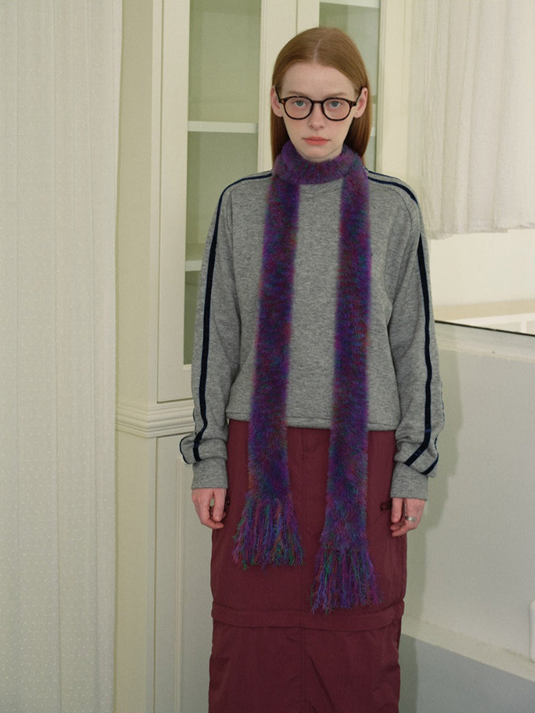 Woman wearing a gray sweatshirt, maroon skirt, white socks, black boots, and a purple and green fuzzy scarf with fringed ends.