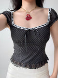 Model wearing a black polka dot print top with a white skirt and red necklace
