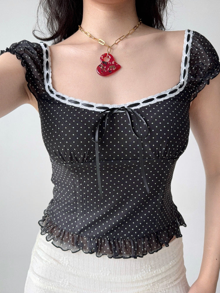 Model wearing a black polka dot print top with a white skirt and red necklace