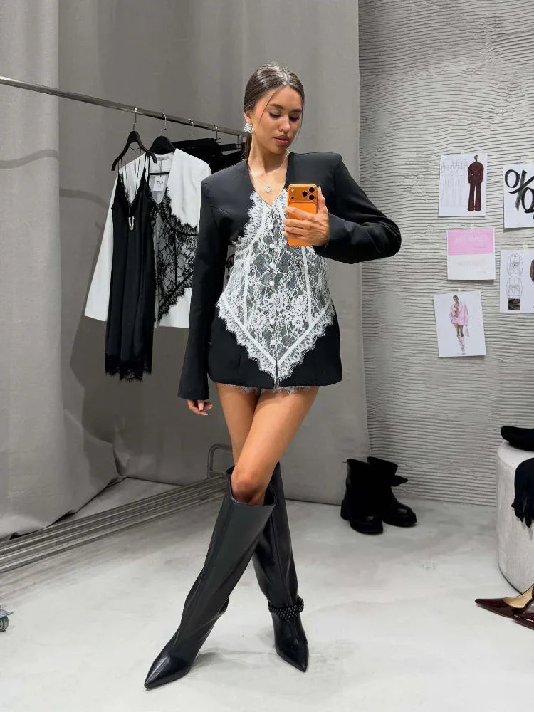 Woman posing in a black blazer dress with a white lace corset overlay and tall black boots