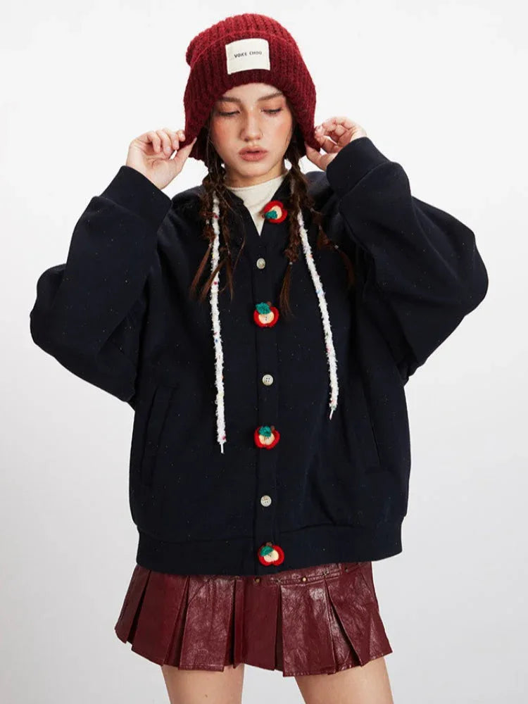 Front view of a woman adjusting her red beanie while wearing a navy blue hooded fleece jacket with apple-shaped buttons.