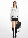 Model wearing a white long-sleeve top with a boat neckline and black shorts.
