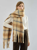 Full body shot of a woman in a white turtleneck and brown pants, accessorized with a plaid scarf