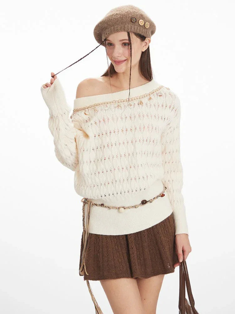 Model adjusting the sleeve of a cream-colored off-the-shoulder knit sweater with a diamond pattern and decorative trim. The sweater is paired with a brown textured mini skirt and a decorative belt.