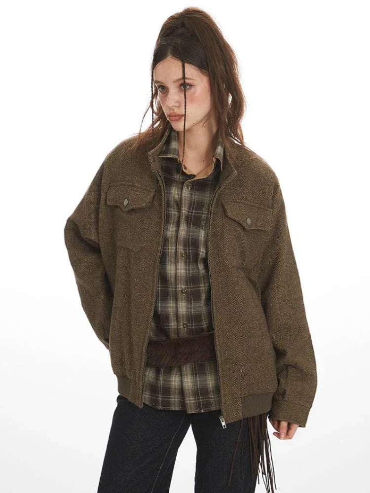 Woman wearing a brown herringbone bomber jacket over a plaid shirt.