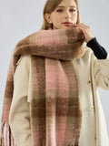 A woman models a cozy plaid scarf in soft pink and brown hues with a brushed texture.