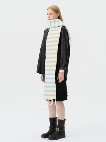 Woman wearing a cream and light blue striped scarf with fringed ends over a black jacket and skirt.