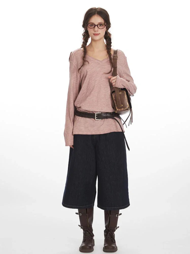 Woman wearing a dusty rose long-sleeve knit top with a V-neck and chest pocket, paired with dark wash wide-leg cropped jeans and brown boots. She has braids and glasses.