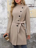 Woman wearing a beige wool blend coat with asymmetrical closure and belted waist