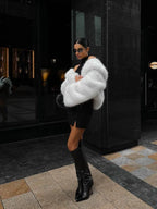Woman wearing a cream faux fur cropped jacket with a black hat and dark wash jeans.
