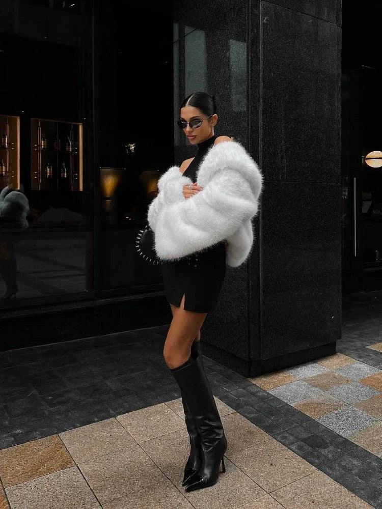 Woman wearing a cream faux fur cropped jacket with a black hat and dark wash jeans.