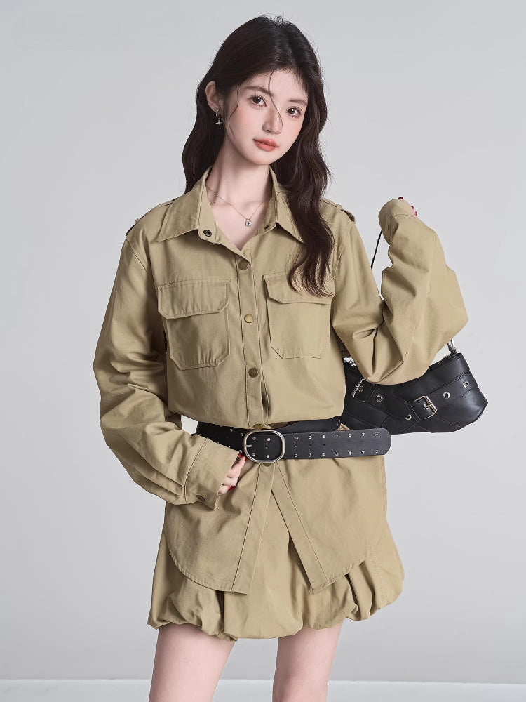 Woman posing with a black shoulder bag, wearing a khaki camp collar shirt dress with long sleeves and a belted waist.