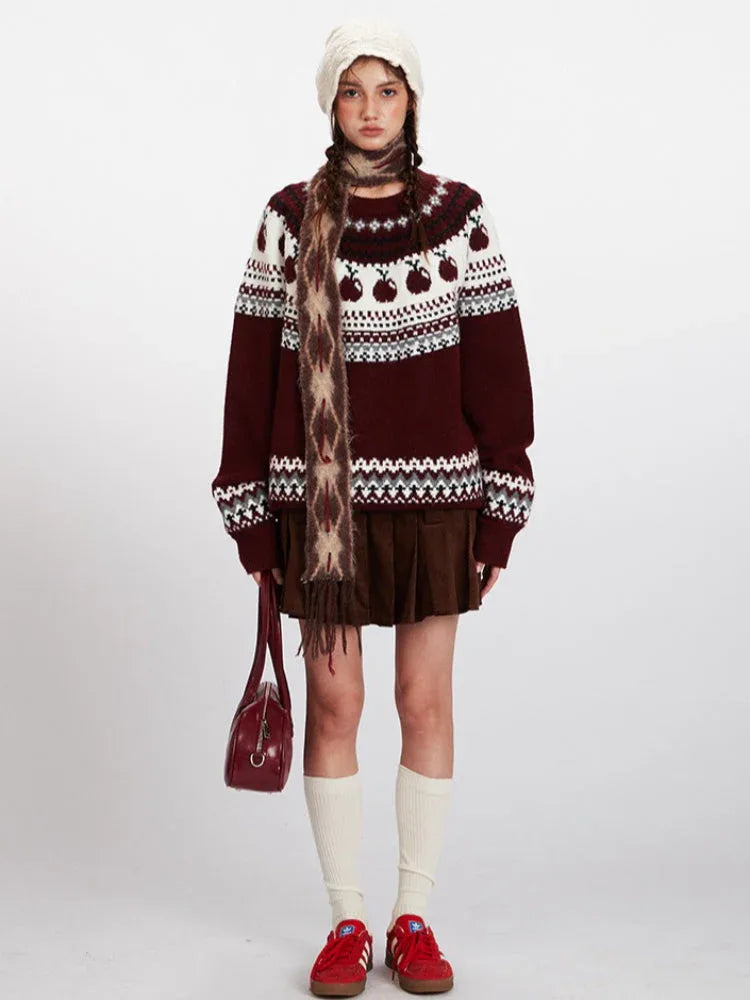 Woman wearing a burgundy Fair Isle crewneck sweater with an apple motif and a white knit hat