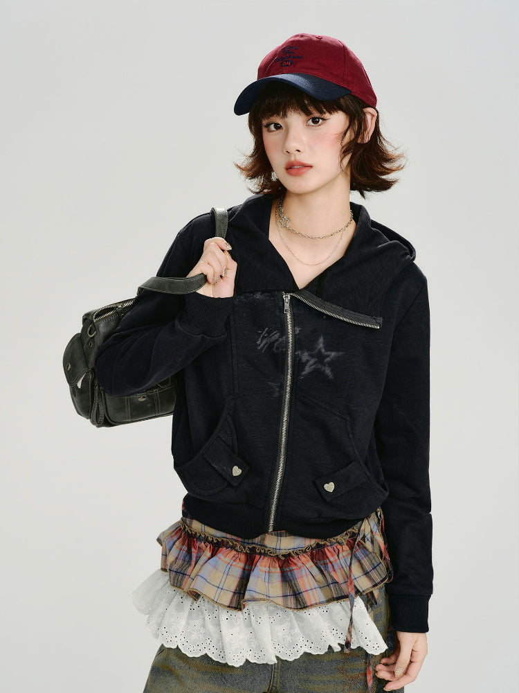 Woman wearing a black zip-up hoodie with a graphic print, a plaid skirt, and a baseball cap.