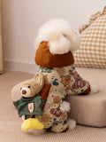 Rear view of a small white dog in a tan patterned dog jacket with a teddy bear applique on the back.