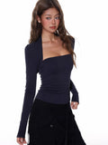 Woman wearing a navy long-sleeve square neck top with a draped overlay, paired with a black skirt.