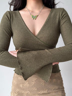 Detail of the flared cuffs and asymmetrical hem of the green ribbed wrap top.