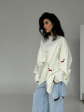 Woman wearing cream oversized knit cardigan with red embroidered dachshunds and denim shorts