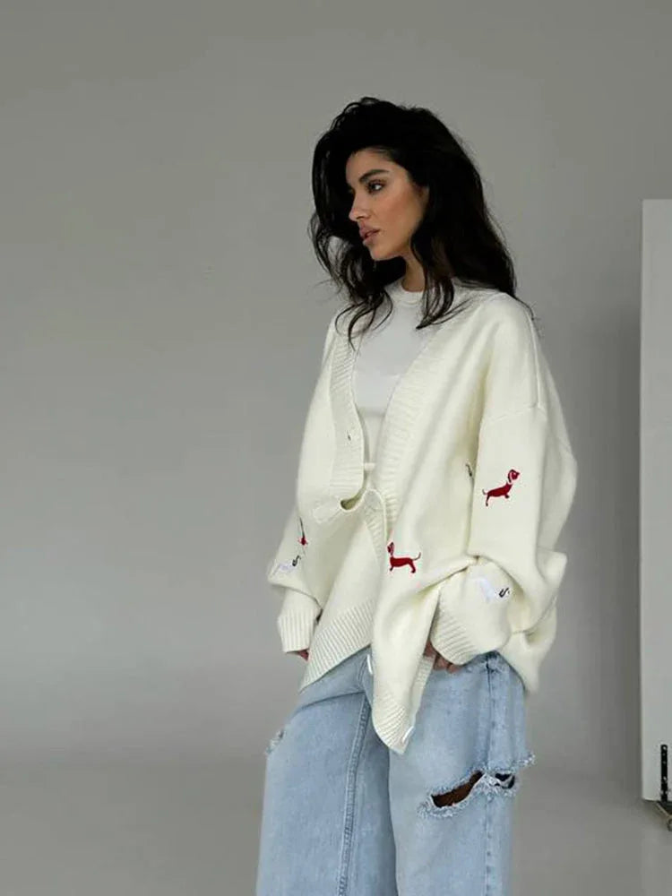 Woman wearing cream oversized knit cardigan with red embroidered dachshunds and denim shorts