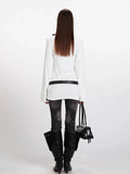 Rear view of a model in a white long-sleeve V-neck top, black belt, and dark wash jeans.