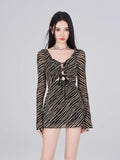 Model wearing a black and gold striped sheer mesh mini dress with long bell sleeves and a tie-front detail.