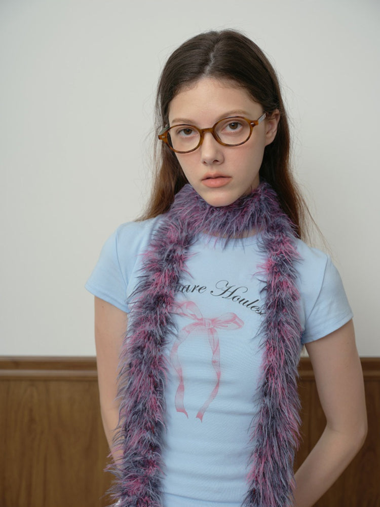 Front view of a woman in a light blue t-shirt and white skirt, accessorized with a statement faux fur scarf.