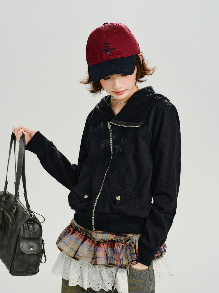 Woman wearing a black zip-up hoodie with a graphic print, a plaid skirt, and a baseball cap.