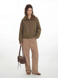 Full-body shot of a woman in a green corduroy bomber jacket, tan pants, and brown shoes, with a brown leather bag.
