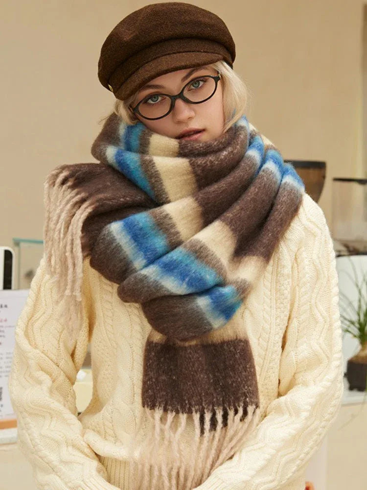 Woman wearing a cream cable knit sweater and a brown plaid scarf with beige, brown, and blue stripes.