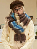 Woman wearing a cream cable knit sweater and a brown plaid scarf with beige, brown, and blue stripes.