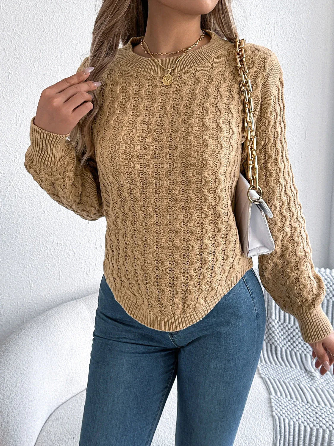 Woman with a white purse slung over her shoulder, wearing a tan textured knit sweater.