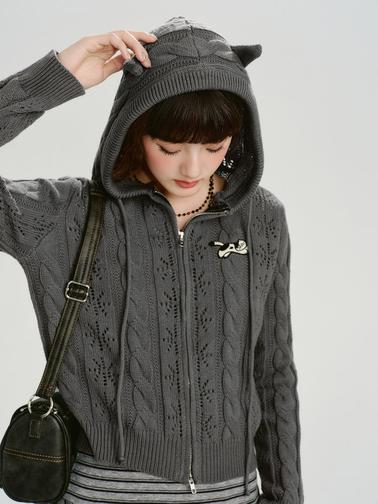 Model adjusting the hood of a grey cable knit cropped hooded jacket with ear details.