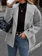Woman wearing a grey double-breasted wool blend pea coat with a black turtleneck and blue jeans, holding a black handbag.