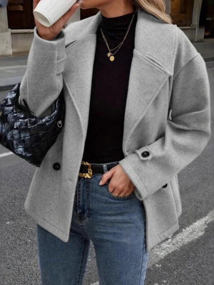 Woman wearing a grey double-breasted wool blend pea coat with a black turtleneck and blue jeans, holding a black handbag.
