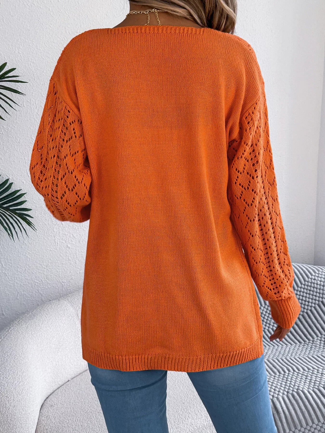 Back view of a woman in an orange open-knit cardigan with long sleeves.