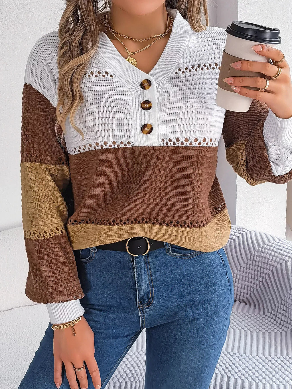 Close-up of a woman holding a coffee cup, wearing a color block knit sweater with a V-neck and button detail.