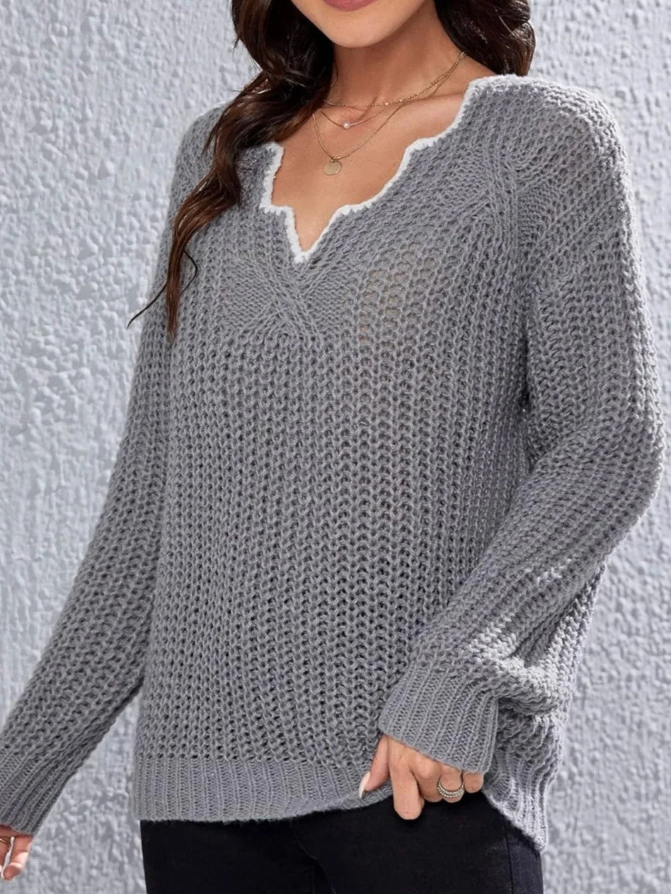 Close-up of the V-neckline of a grey knit sweater with decorative trim.