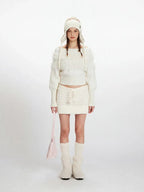 Woman wearing a white off-the-shoulder knit sweater with fuzzy trim and a matching white knit mini skirt with a drawstring waist.