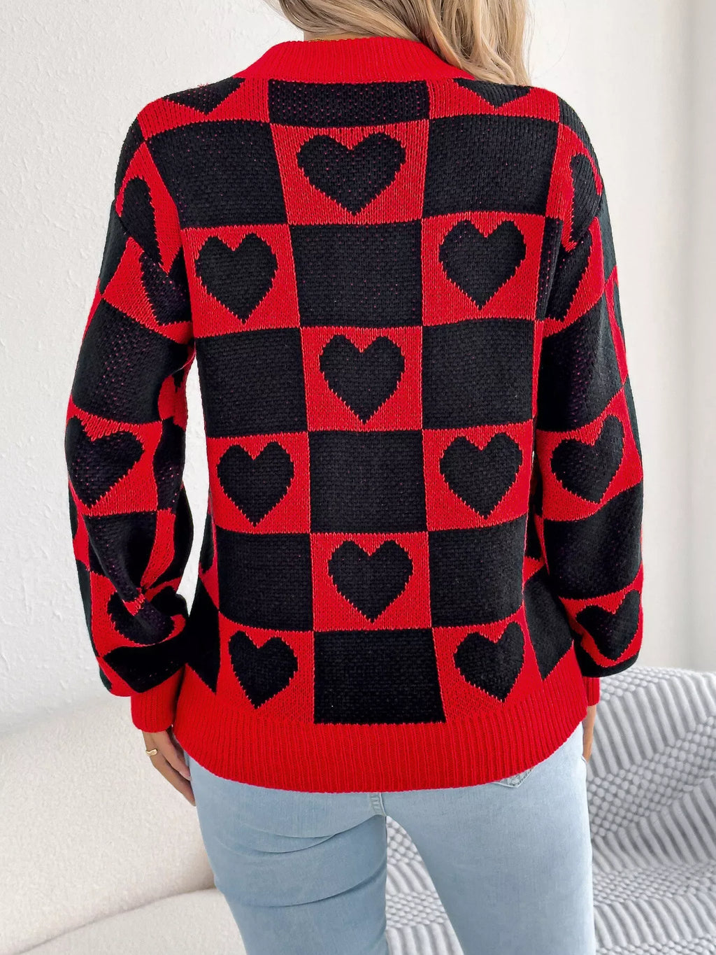 Back view of a woman wearing a red and black checkerboard knit sweater with black heart patterns.