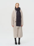 Woman wearing a dark stripe scarf with fringed ends over a beige cardigan and culottes.