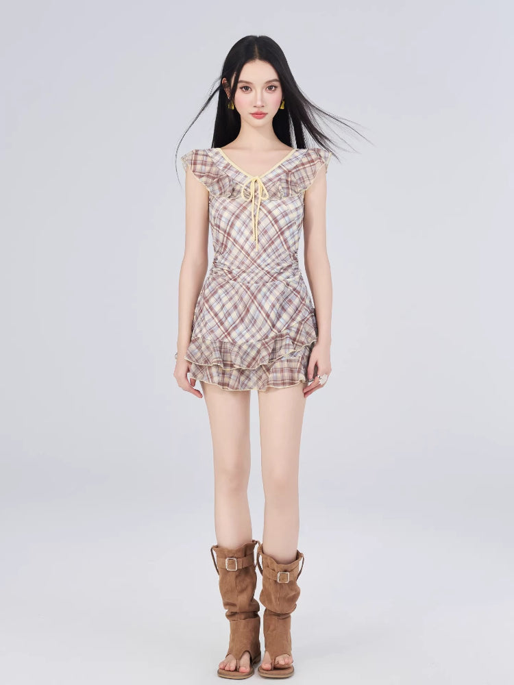 Woman wearing a plaid print, v-neck, cap sleeve dress with ruffled neckline and tiered ruffle hem.