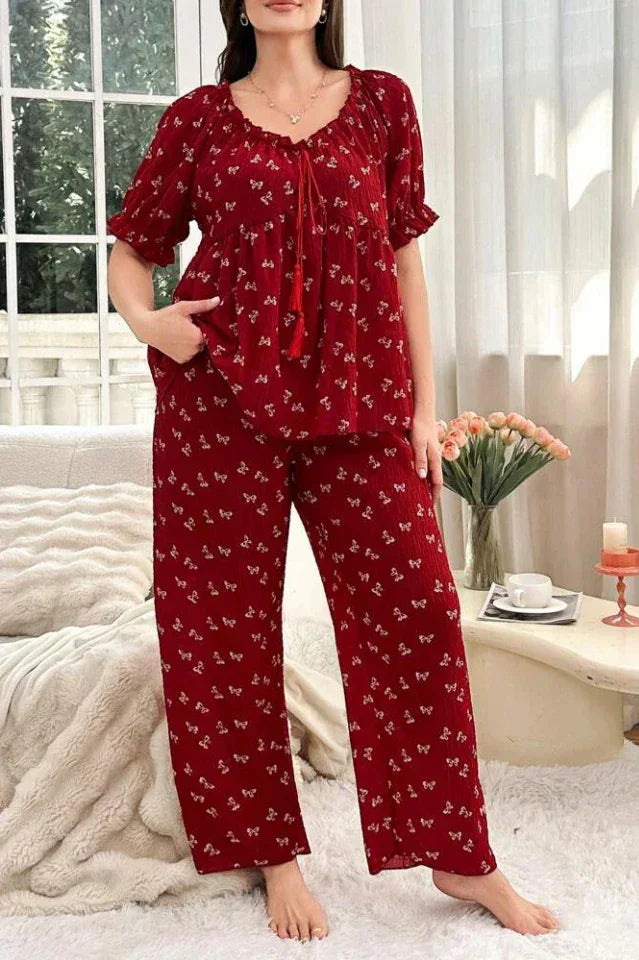 Woman wearing a red pajama set with a white butterfly print, featuring a tie-neck top and wide-leg pants.