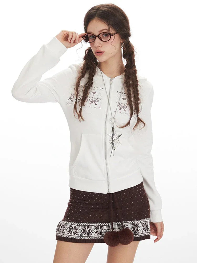 Close-up of a woman wearing a white hooded zip-up jacket with a bow and heart graphic print, showing the zipper detail and necklace.