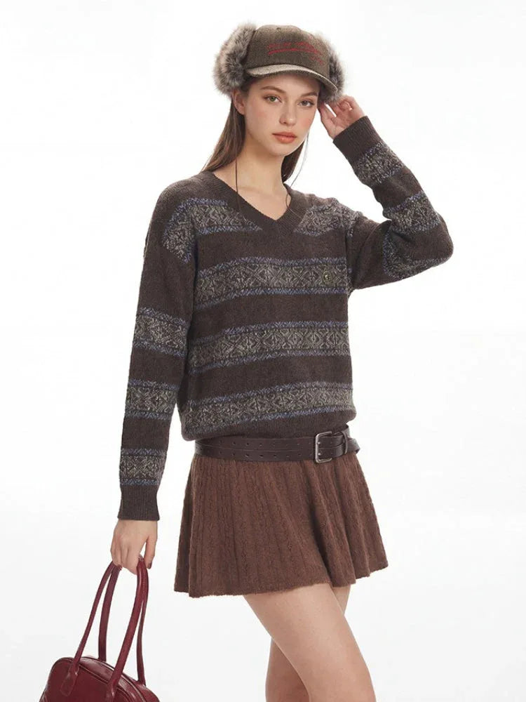 Woman smiling while adjusting her hat, wearing a brown V-neck knit sweater with patterned stripes.