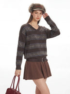 Woman smiling while adjusting her hat, wearing a brown V-neck knit sweater with patterned stripes.
