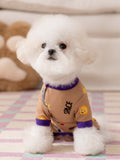 Small white dog wearing a tan dog pajama with a space print and purple trim