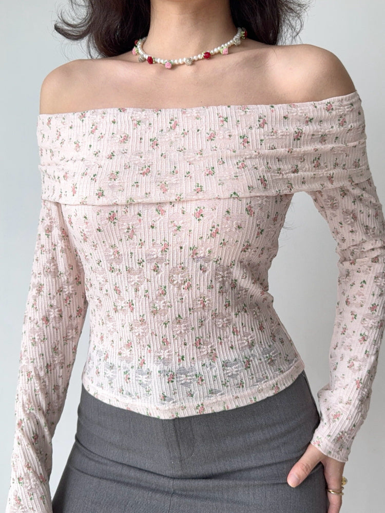 Close-up of a woman wearing a pink off-the-shoulder floral print top with textured fabric and long sleeves.